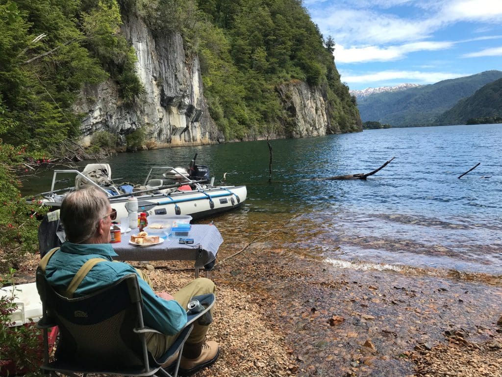 Man relaxing by lakeside with boats nearby.