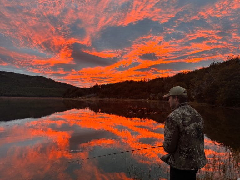 Fisherman at sunset with vibrant sky reflection.