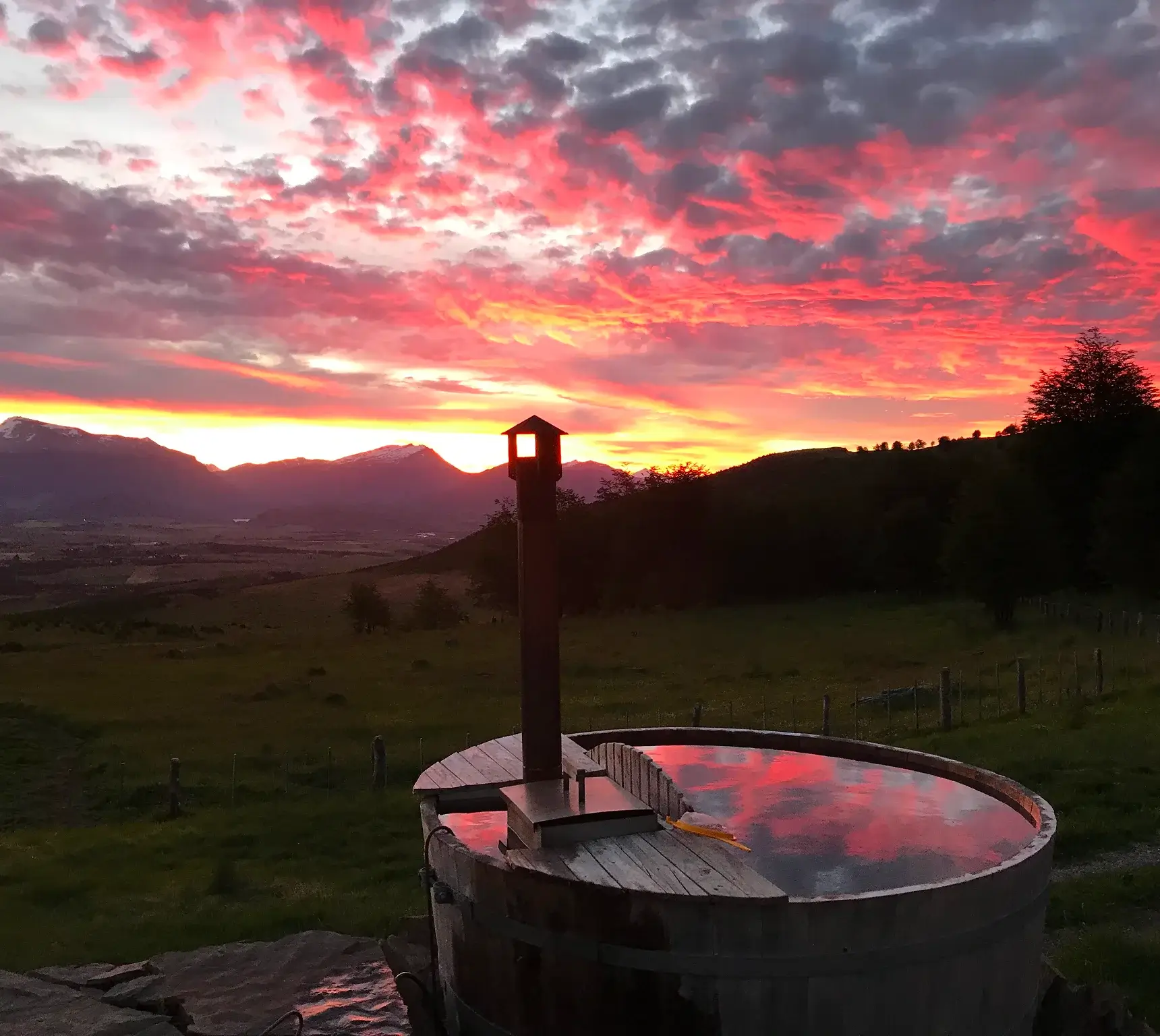 Sunset with a vibrant pink sky over mountains and a metal water container in the foreground.
