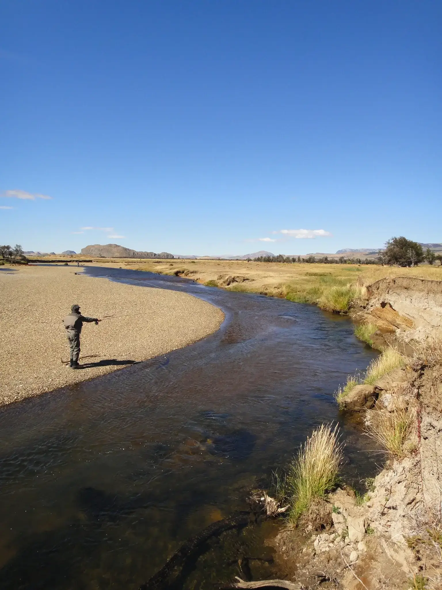 Person fishing by a winding river in a dry landscape.